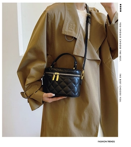Detail of black quilted leather bucket bag featuring gold dual zippers and a reinforced handle