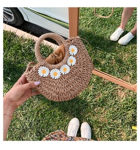Dettaglio di una borsa a mano semicircolare in paglia con margherite bianche sull'erba