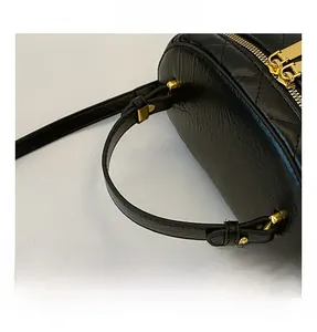 Detail view of black quilted cylinder handbag featuring golden zipper and leather texture