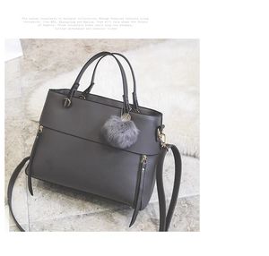 Detail of dark grey tote bag with smooth leather finish, gold zippers and faux fur pompom