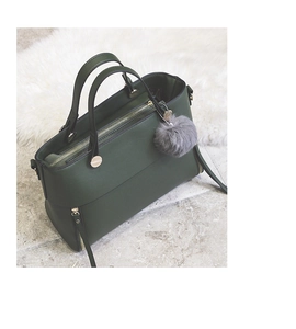 Detail of dark green leather handbag with soft grey fur ball charm and metal zipper