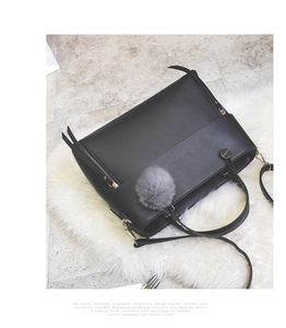 Detail of black tote bag with gold zippers and grey fur ball charm on white faux fur rug