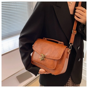 Close-up of brown vintage PU leather handbag with bronze twist lock on a female model