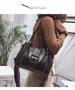 Detail of black bucket bag with white contrast stitching and a striped woven strap