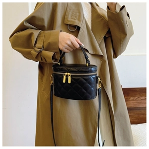 Detail of a black quilted mini box bucket bag with gold zippers and a slim shoulder strap