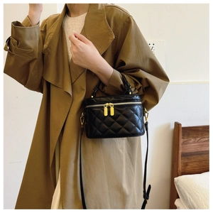 Detail of black quilted box bag with gold dual zippers and adjustable shoulder strap