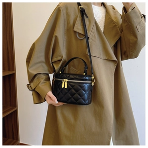 Detail of black quilted bucket bag with gold zippers worn with a stylish trench coat