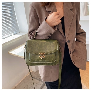 Detail of vintage moss green PU leather bag with bronze lock on model in brown suit