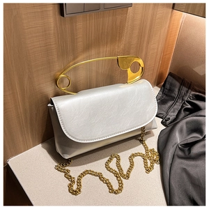 Detail view of a silver flap bag featuring a large gold safety pin handle and chain strap