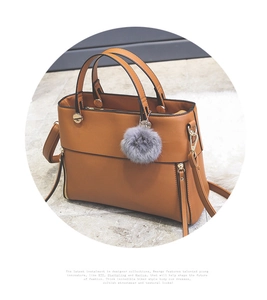 Detail of a brown tote bag with grey pompom charm and golden decorative side zippers