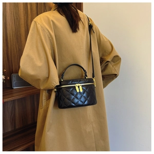 Detail of black quilted bucket bag with gold hardware worn over a khaki trench coat