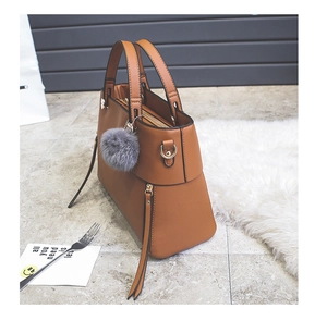 Detail view of caramel faux leather tote bag with tassel zipper and grey fur ball charm
