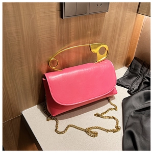 Detail of rose pink handbag featuring a unique gold oversized safety pin handle and chain