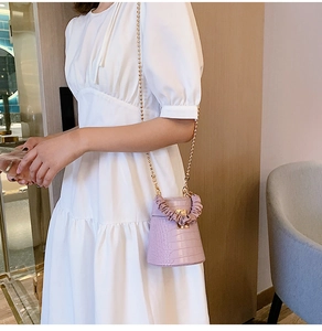 Detail of purple crocodile pattern bucket bag with gold chain strap on white dress