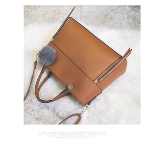 Detail of a brown leather tote bag with gray faux fur pom-pom charm and top handles