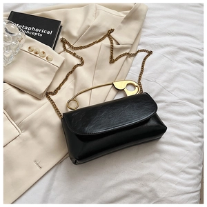 Detail of glossy black handbag featuring creative gold safety pin handle and chain strap