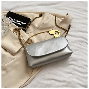 Detail of silver crossbody bag featuring a unique oversized gold safety pin handle and chain