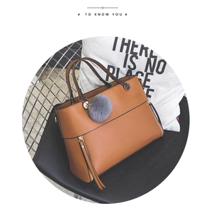 Close-up of brown leather tote bag featuring gold hardware and a grey faux fur keychain