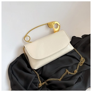 Detail of white leather bag featuring unique gold safety pin handle and metal chain
