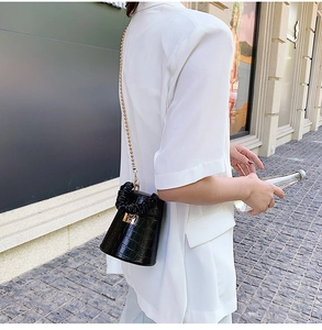 Detail of black crocodile pattern bucket bag with gold lock and chain on white shirt
