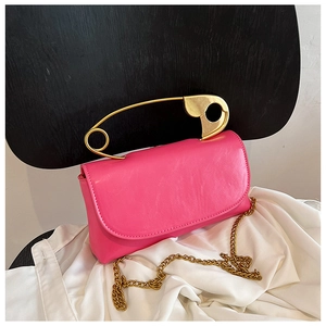 Close-up of rose pink handbag with gold safety pin handle and chain strap on chair