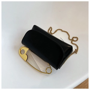 Detail of black flap bag featuring golden safety pin ornament and fine chain strap