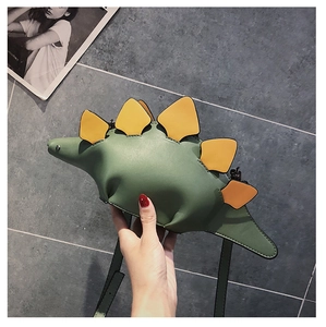 Close-up of green dinosaur-shaped crossbody bag with yellow spikes held by a hand