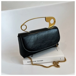 Close-up of black textured leather bag featuring a unique large golden safety pin handle