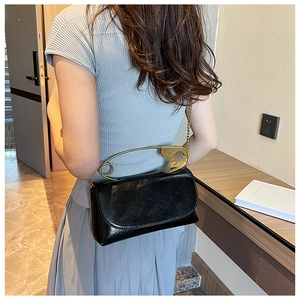 Chic black patent shoulder bag with unique gold safety pin handle shown on model