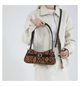 Detail of orange snakeskin textured baguette bag with gold buckle and black strap