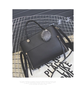 Close-up of black leather tote with gold zippers and grey pom-pom charm on a chair