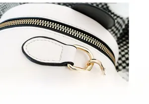 Detail view of the golden metal hook and black zipper on the white leather round bag