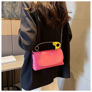 Pink glossy crossbody bag featuring unique gold safety pin handle and metal chain strap