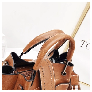 Detail of caramel leather bag showing grainy texture, silver rivets, and white stitching