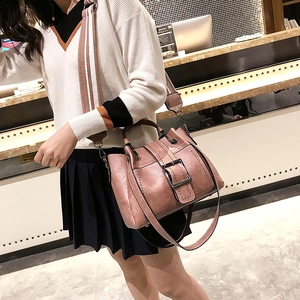 Detail of pink faux leather bag featuring a wide striped shoulder strap and metal buckle
