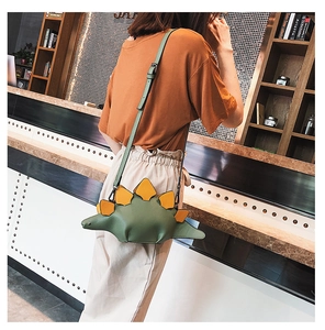Detail of creative green dinosaur crossbody bag with yellow spikes worn over shoulder