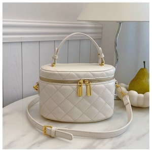 Detailed view of cream quilted bucket bag with gold zippers on a marble surface