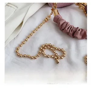 Detail of pink crocodile pattern bucket bag with golden ball chain and gathered handle