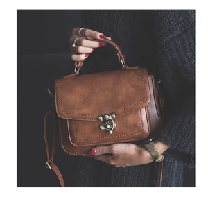 Close-up of vintage brown PU leather handbag featuring a bronze twist lock and metal hardware