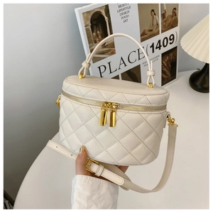 Detail of cream quilted handbag featuring gold dual zippers and adjustable shoulder strap