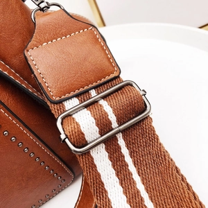 Close-up of brown leather bag featuring striped textile strap and silver metal buckle