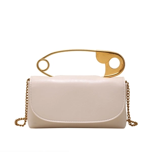 Elegant cream shoulder bag featuring a unique oversized gold safety pin handle and chain