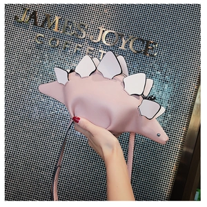 Close-up of pink dinosaur shaped crossbody bag with white triangular scales and strap