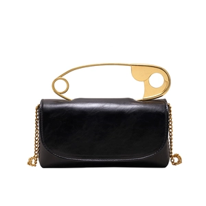 Modern black leather tote bag with unique oversized gold safety pin handle and chain strap