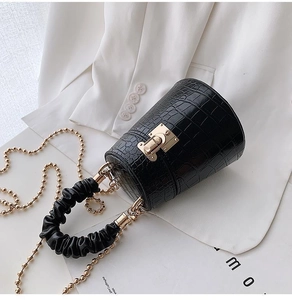 Black crocodile pattern bucket bag with gold lock and chain on white blazer background