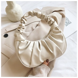 Detailed view of cream pleated dumpling bag on beige suit jacket with minimalist decor