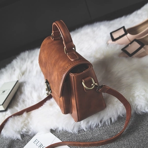 Retro brown leather handbag with gold metal clasp on white faux fur background