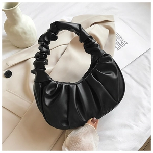 Close-up of black pleated dumpling bag with soft cloud texture on beige blazer background
