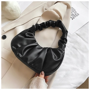 Close-up of black ruched croissant bag with matte texture on beige blazer