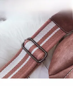 Detail of striped woven shoulder strap with gunmetal buckle on dusty rose suede bag
